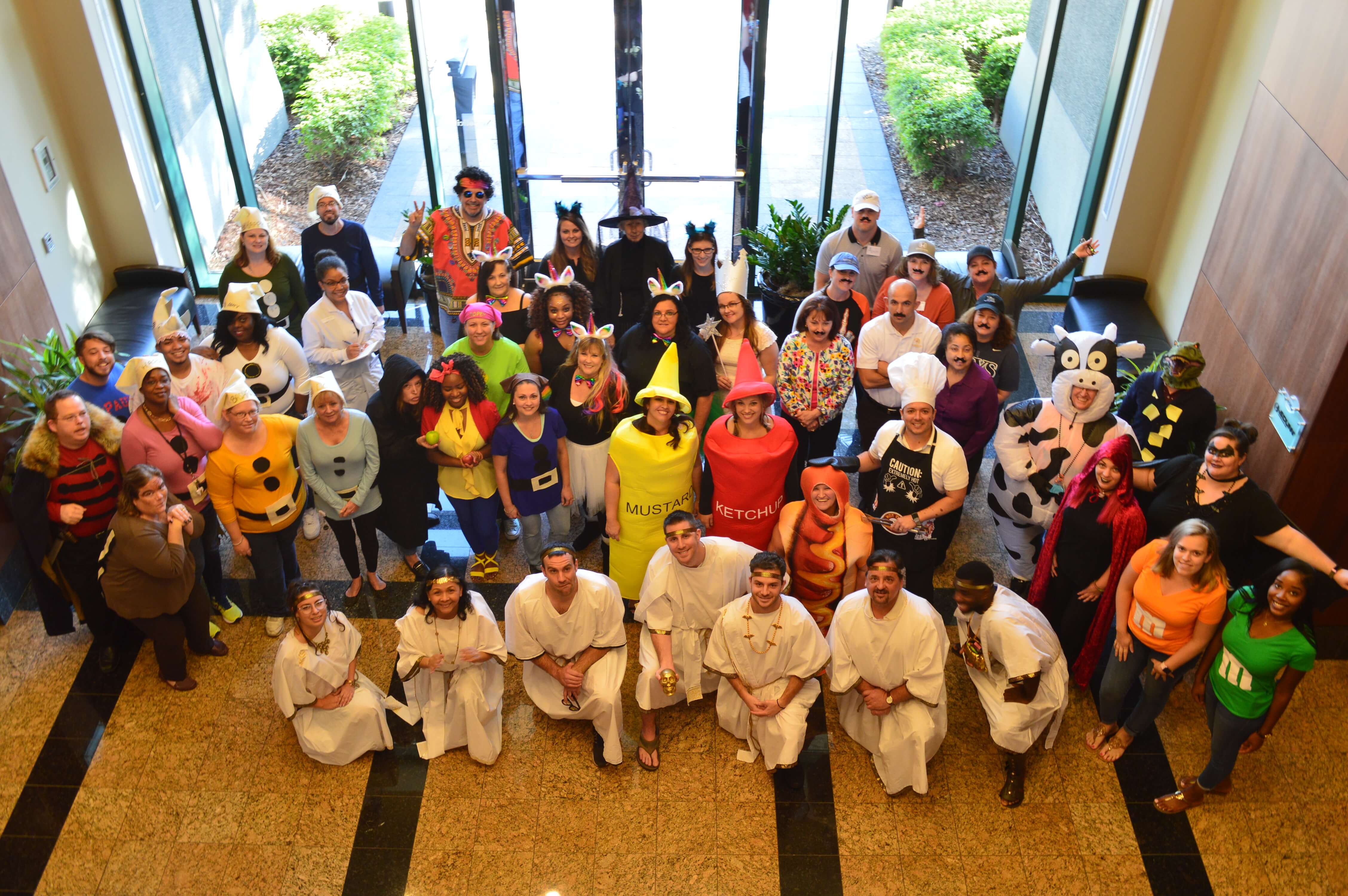 Employees of American Integrity in various Halloween costumes standing and smiling in the lobby of their office building