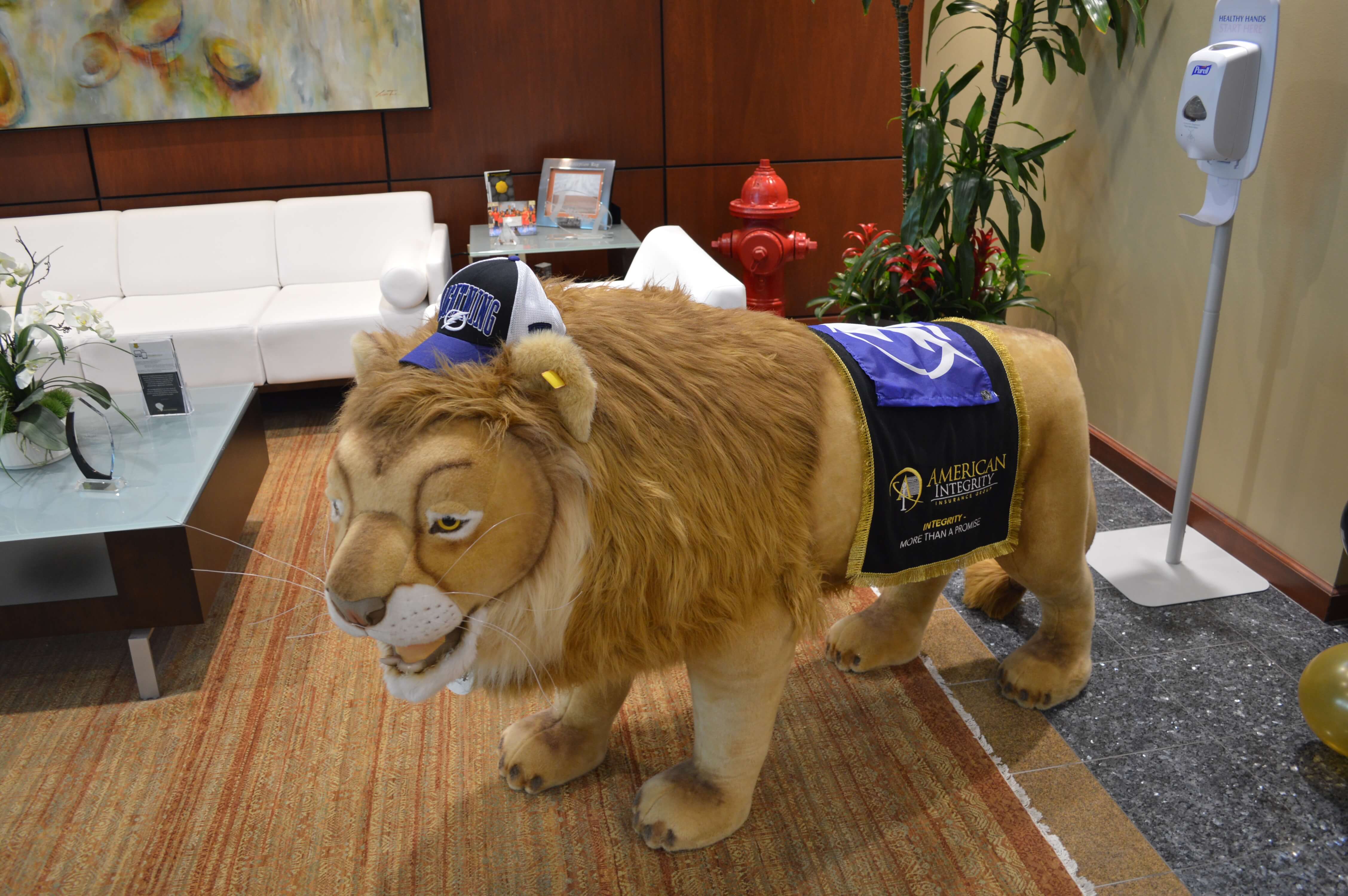 Life-sized version of Leo the Lion in the front lobby of American Integrity's offices, wearing a Tampa Bay Lightning baseball cap and flag